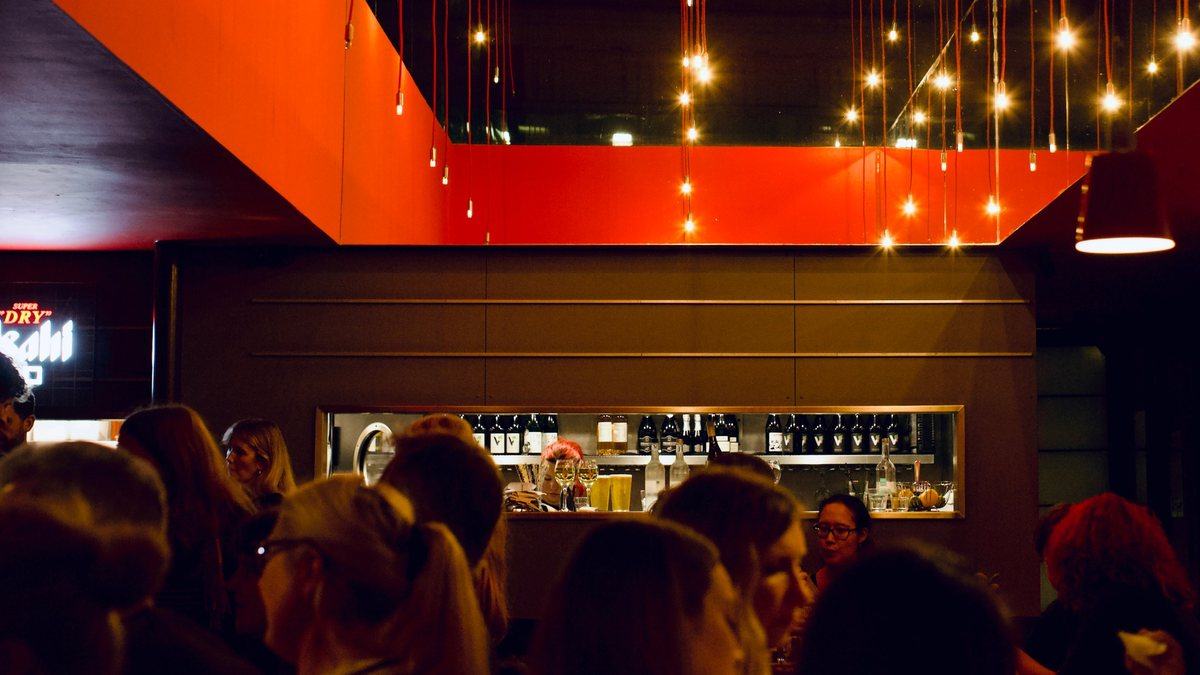 The bar under the red ceiling and hanging lights, busy on a weekend night