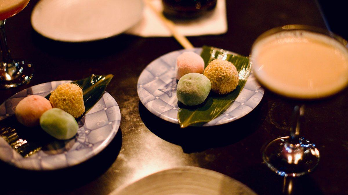 Mochi on belt plates beside two cocktails at the counter