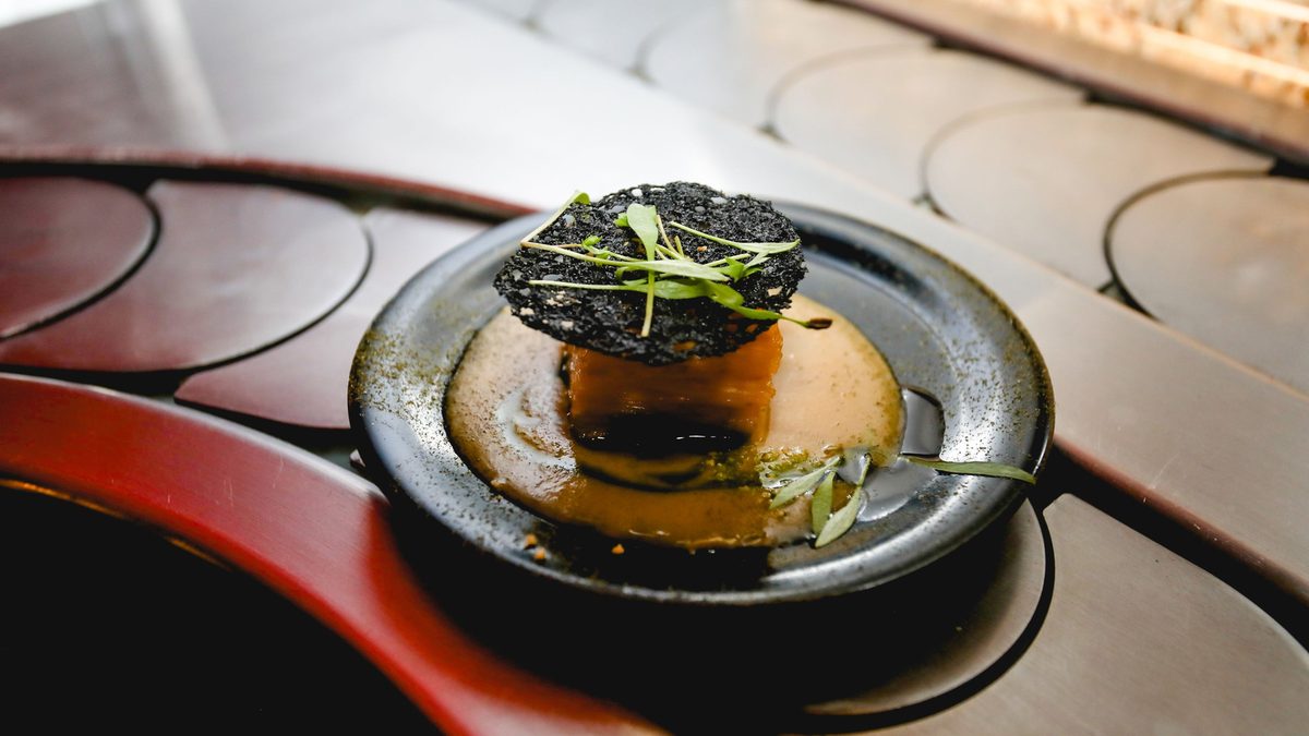 A plant-based plate on the belt, crisp black tuile and fresh shoots over a golden sauce